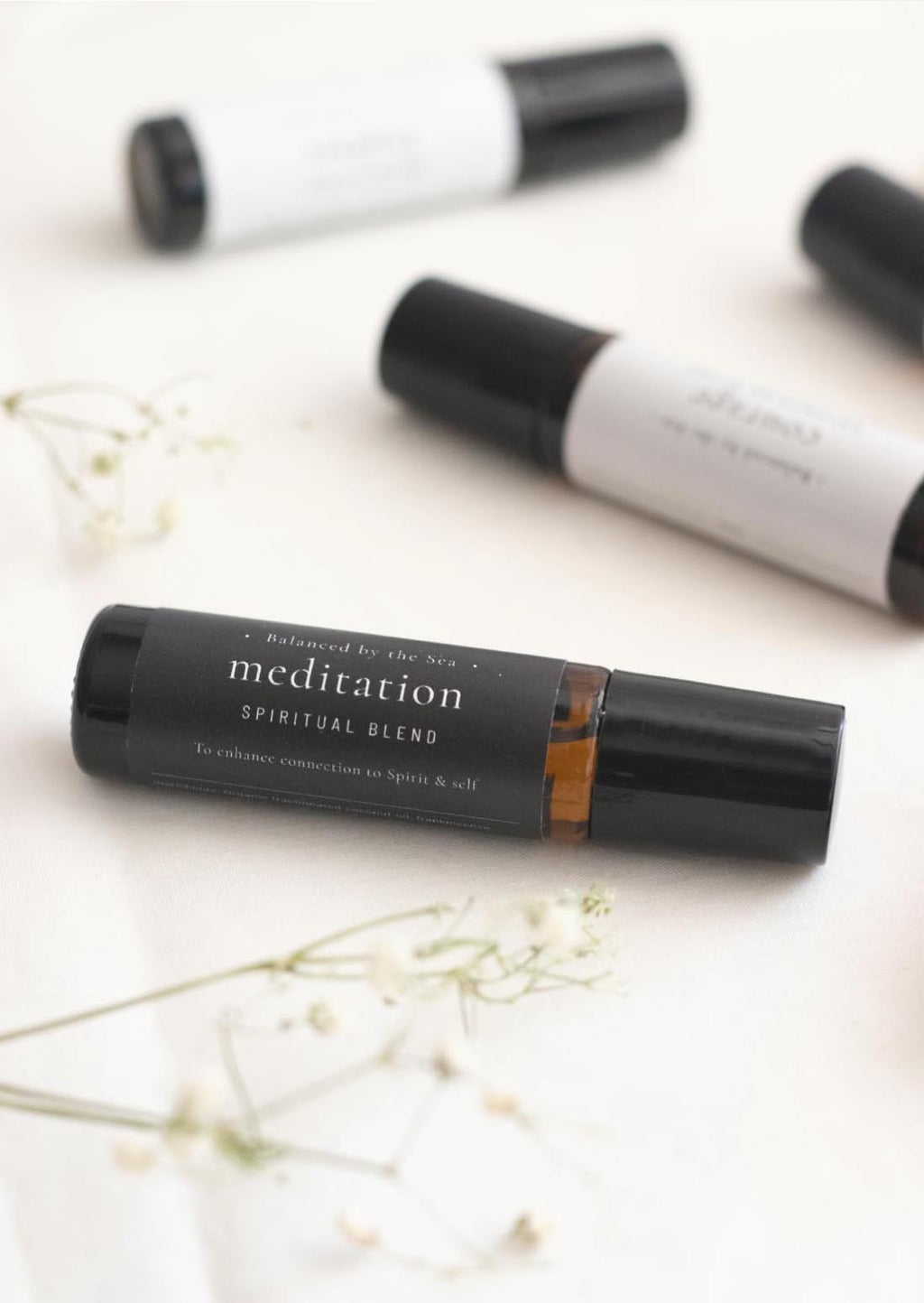 Three amber Balanced by the Sea essential oil roller bottles are displayed on a white surface with a white marble background.