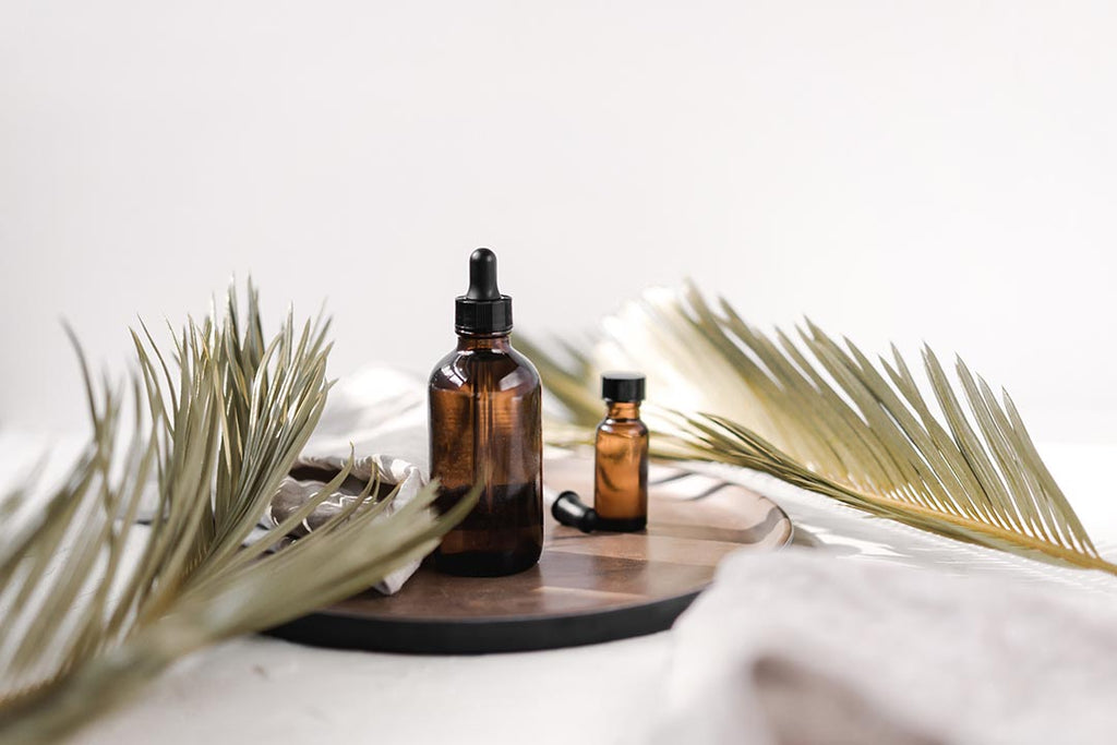 amber bottles containing essential oils are arranged on a wooden centrepiece. around them, palm leaves and organic linen cloths are scattered in an aesthetically pleasing way 