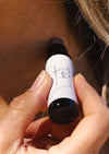 A person is applying a luxurious aromatherapy essential oil blend to their neck using an amber Balanced by the Sea roller bottle
