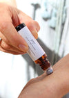 A person is applying a luxurious aromatherapy essential oil blend to their wrist using an amber Balanced by the Sea roller bottle