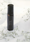 An amber essential oil roller bottle is standing on a white tablecloth, surrounded fine white gypsum flowers. It has a black cap and a black Balanced by the Sea label with the words "Clarity - Focus Blend" on it