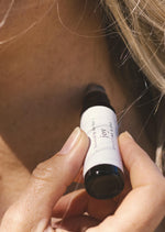 A person is applying a luxurious aromatherapy essential oil blend to their neck using an amber Balanced by the Sea roller bottle