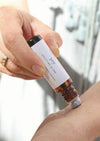 A person is applying a luxurious aromatherapy essential oil blend to their wrist using an amber Balanced by the Sea roller bottle