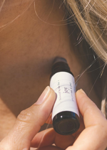 A person is applying a luxurious aromatherapy essential oil blend to their neck using an amber Balanced by the Sea roller bottle