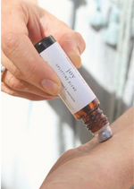 A person is applying a luxurious aromatherapy essential oil blend to their wrist using an amber Balanced by the Sea roller bottle